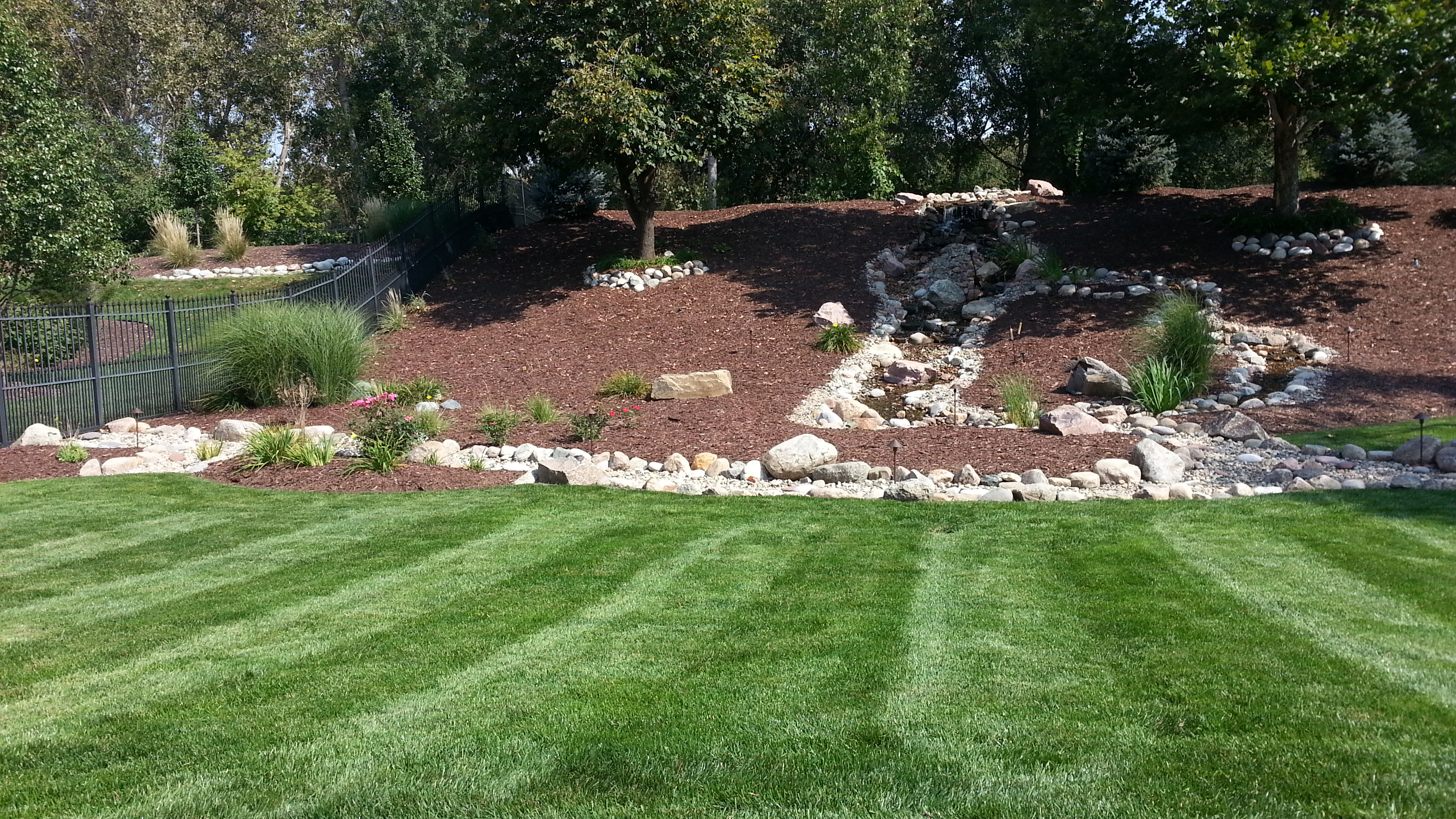 A freshly striped, healthy green lawn with manicured landscaping, maintained by HP Lawn and Snow in Omaha